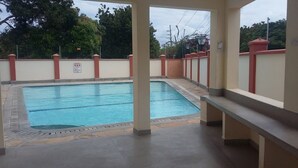 A rectangular swimming pool with a tiled edge, surrounded by a low wall with red and beige pillars.