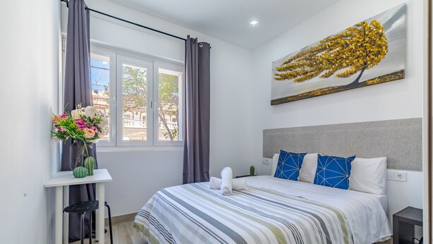 A modern hotel room with a large bed, a desk with a vase of flowers, and a window with curtains. - AYZ Silvela - Auto check-in property (Málaga)