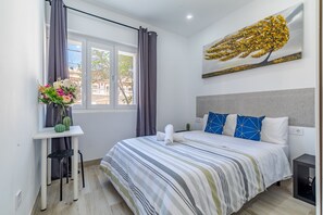 Une chambre d’hôtel moderne avec un grand lit, un bureau agrémenté d’un vase de fleurs et une fenêtre avec des rideaux.