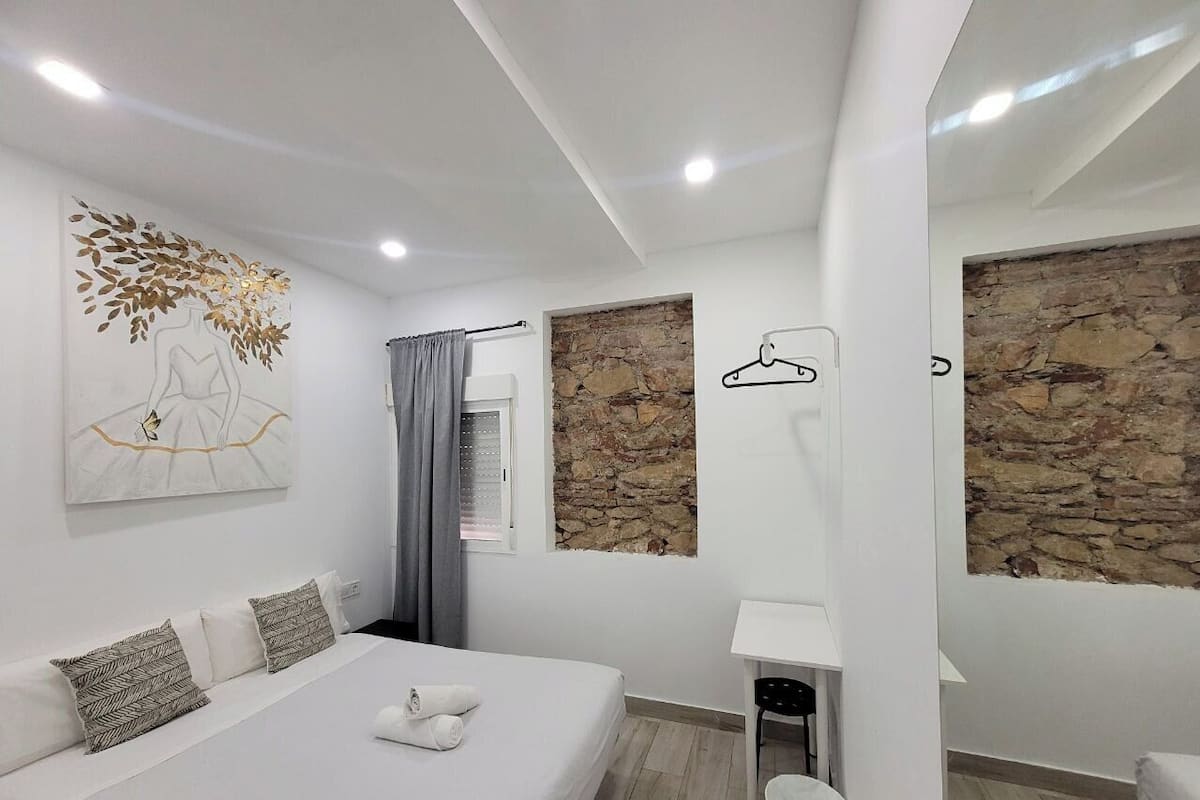 A modern bedroom with a large bed, a desk, and a stone wall.
