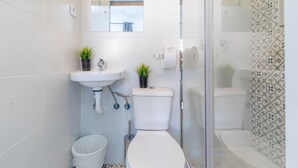 A modern bathroom with a white sink, two toilets, a glass shower enclosure, and patterned wall tiles. - AYZ Silvela - Auto check-in property (Málaga)