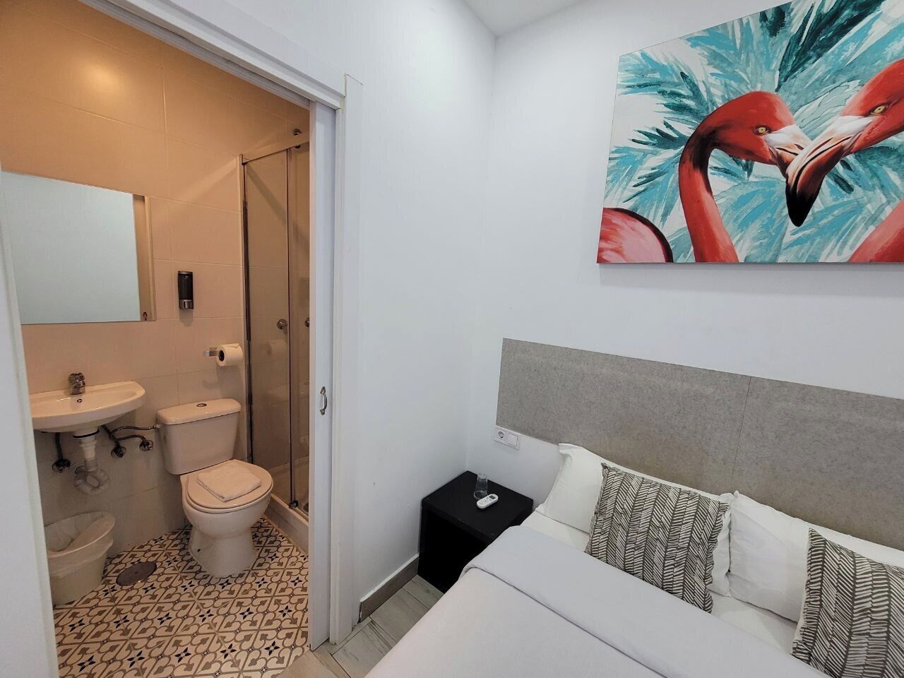 Hotellihuone, jossa on sänky, yöpöytä ja kylpyhuone, jossa on wc, pesuallas ja suihku.