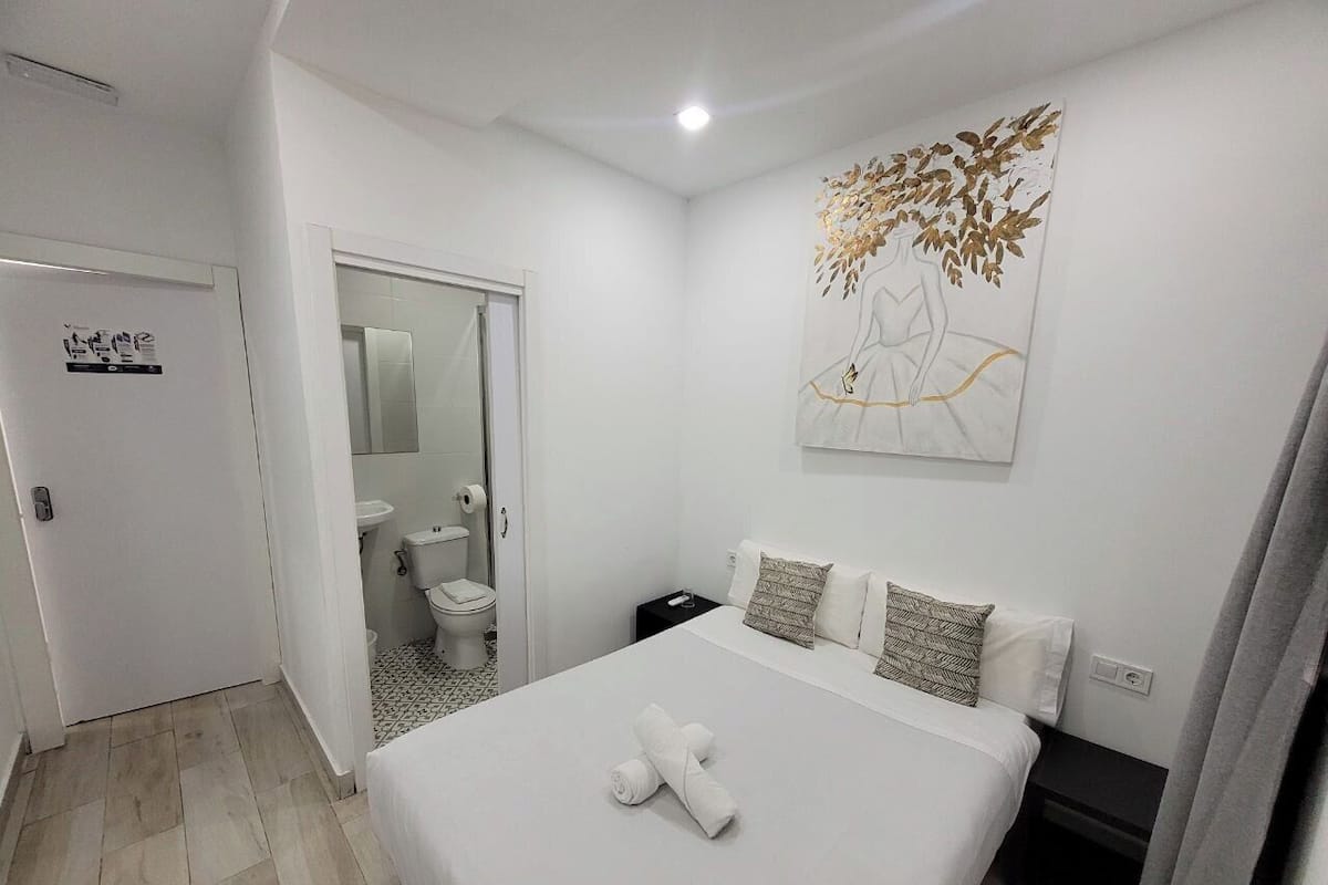 A hotel room with a bed, a bathroom, and a painting on the wall.