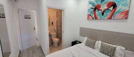 Een hotelkamer met een bed, een badkamer met toilet en douche, en een flamingo schilderij aan de muur.