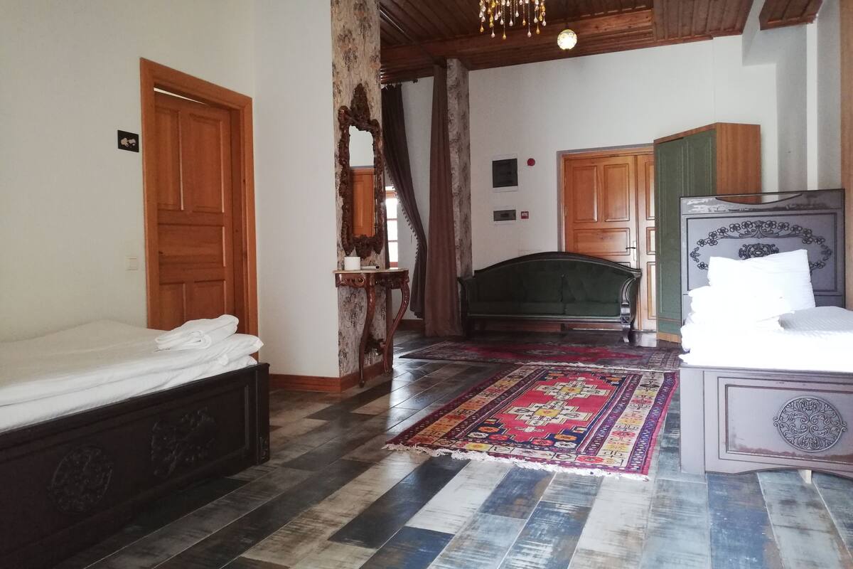 A room with a bed, a green sofa, a wooden ceiling, and a patterned rug.