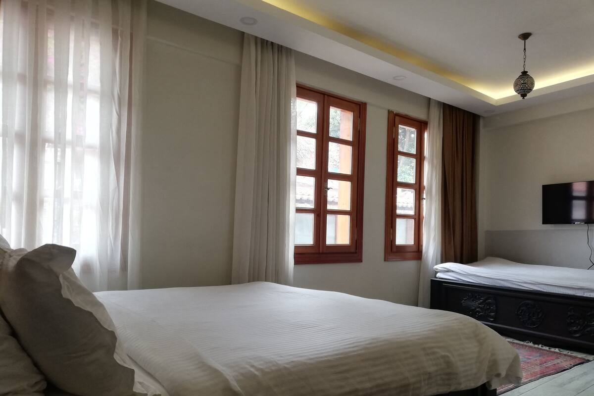 A hotel room with a bed, a television, and two windows with curtains.