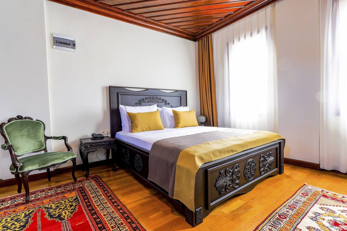 A bedroom with a wooden bed, a green chair, a nightstand, and a patterned rug.
