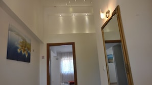 Un pasillo con un cuadro, un espejo y una puerta que da a una habitación con cama y mesa.