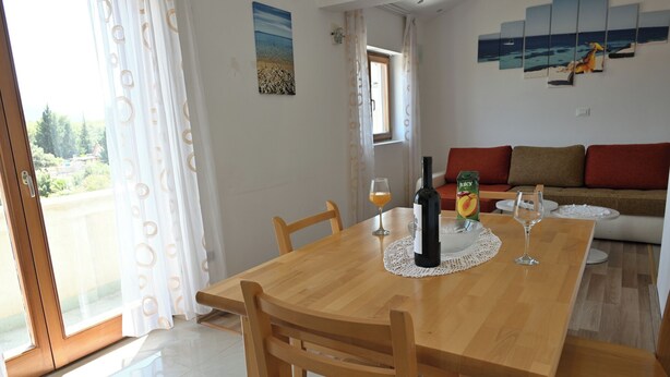 Un comedor con una mesa de madera, sillas, una botella de vino, un vaso de jugo y un cuadro en la pared.