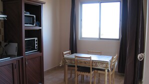 A small kitchen with a microwave, a cabinet, a dining table with chairs, and a window with curtains. - COTOMILI ACCOMMODATION WITH SWIMMING POOL (Trou aux Biches)