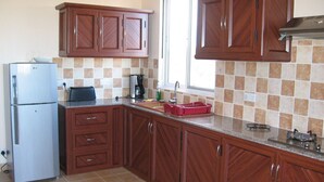 A kitchen with wooden cabinets, a stainless steel refrigerator, a window, and a tiled backsplash. - COTOMILI ACCOMMODATION WITH SWIMMING POOL (Trou aux Biches)