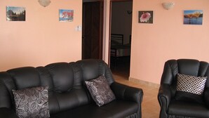 A living room with a black leather sofa and armchair, two wall-mounted light fixtures, and three framed pictures on the wall. - COTOMILI ACCOMMODATION WITH SWIMMING POOL (Trou aux Biches)