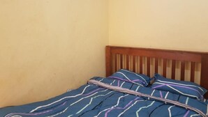 Una habitación pequeña con cama individual, cabecera de madera y pared lisa.