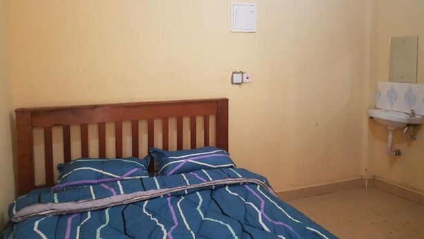 Un dormitorio con cama de madera, colcha azul estampada, enchufe de pared y un lavamanos blanco pequeño con espejo encima.