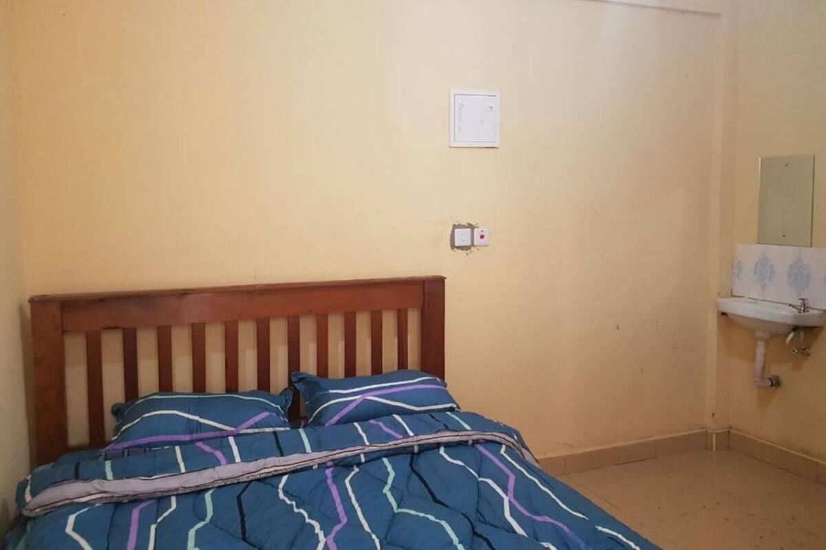 Quarto com cama de madeira, colcha de cama estampada em azul, tomadas na parede e pia pequena branca com espelho acima.
