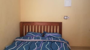 Una cama individual con cabecera de madera en una habitación con paredes lisas de color amarillo.