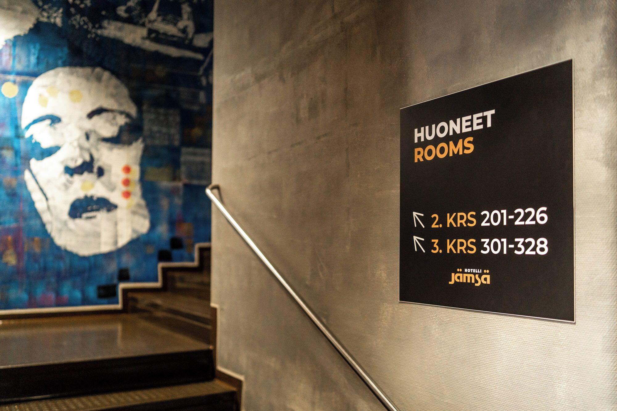 Letrero en la pared que indica 'HUONEET ROOMS' con flechas direccionales y números de teléfono para acceder a las habitaciones.