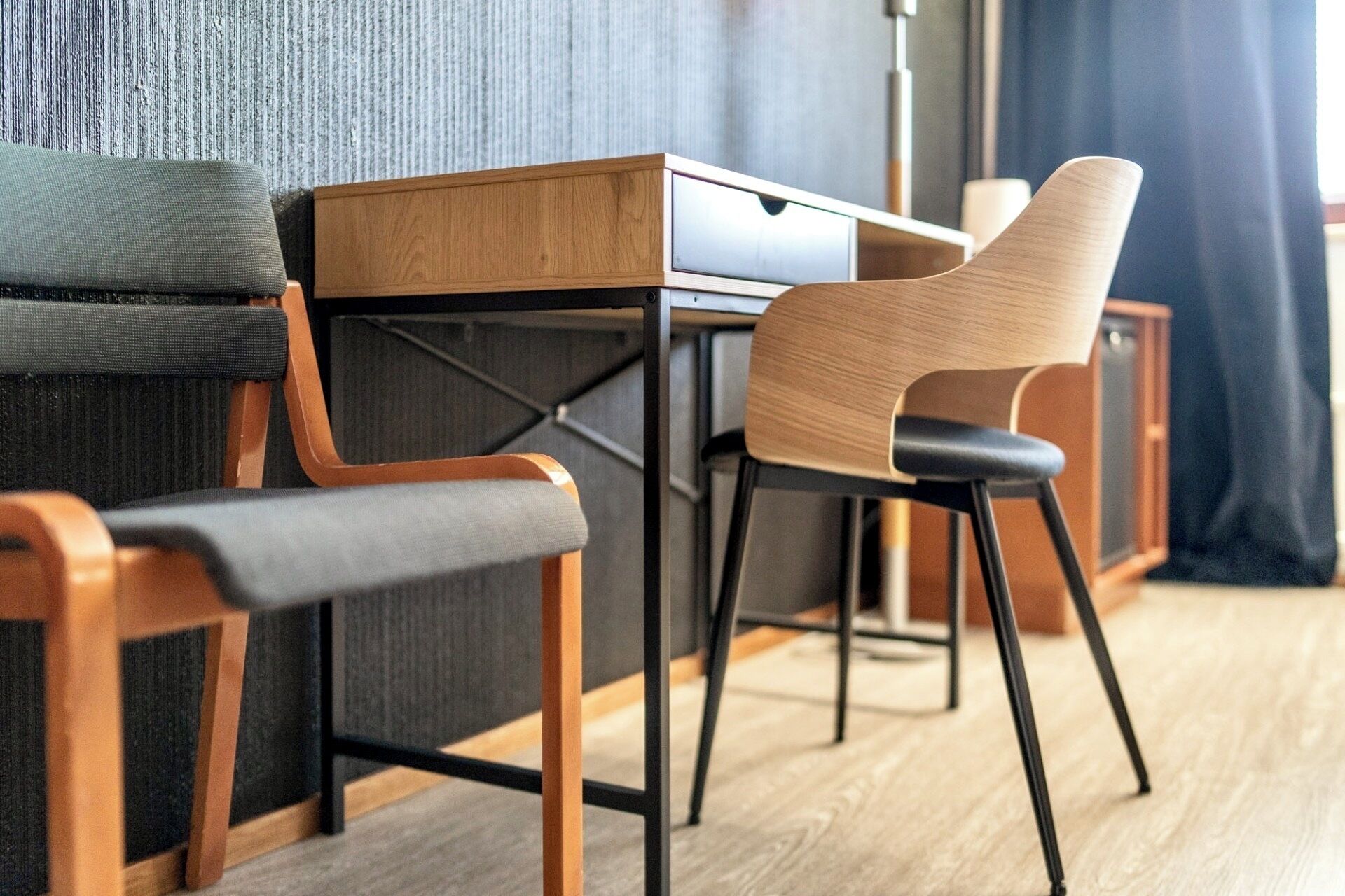 A modern room with a wooden desk, a grey sofa, and a wooden chair.