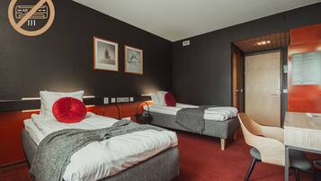 A hotel room with two beds, a desk, a chair, a door, and a wall-mounted control panel.