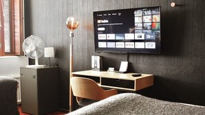 Una habitación de hotel con un televisor en la pared, un escritorio con una silla, un ventilador y un armario.
