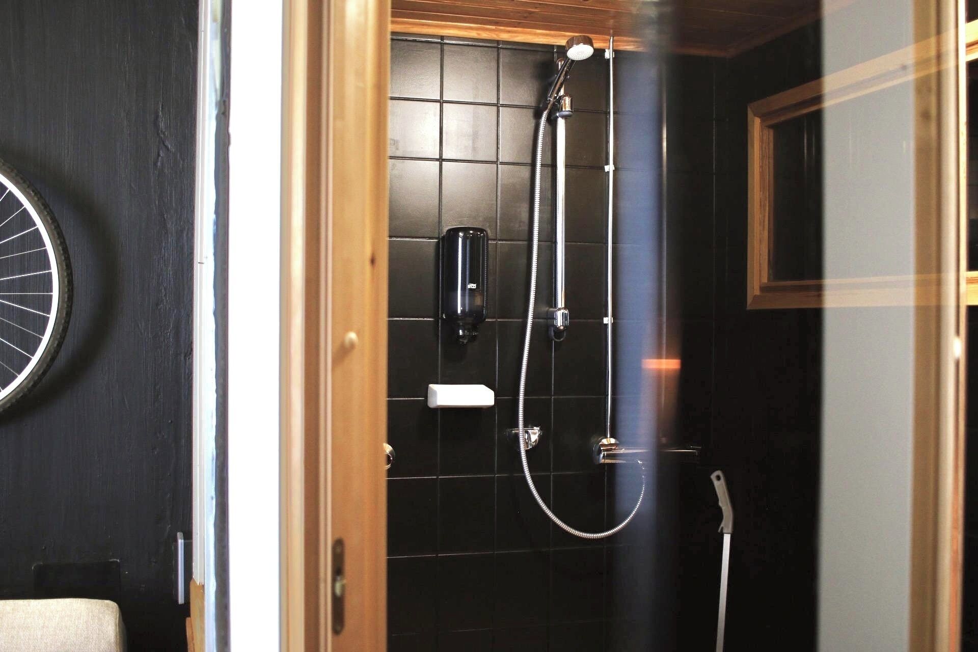 Een douche met een handdouche en een handscrubber, een handdoekhouder en een raam met houten kader.