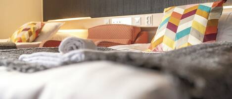 A hotel room with a bed, pillows, a blanket, and a wall-mounted light switch.