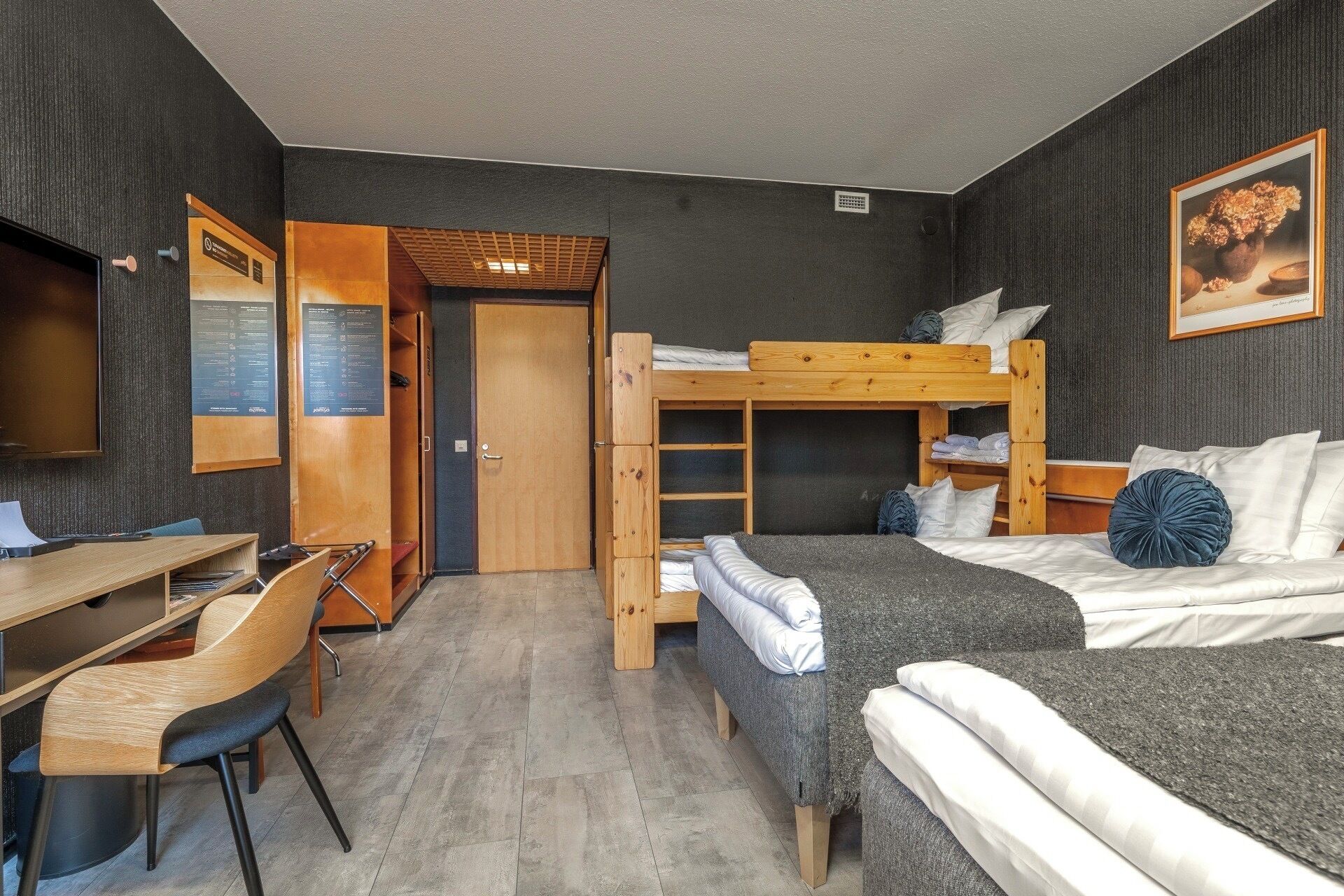 Habitación de hotel compacta con una cama litera, un escritorio con silla, un armario y un televisor.
