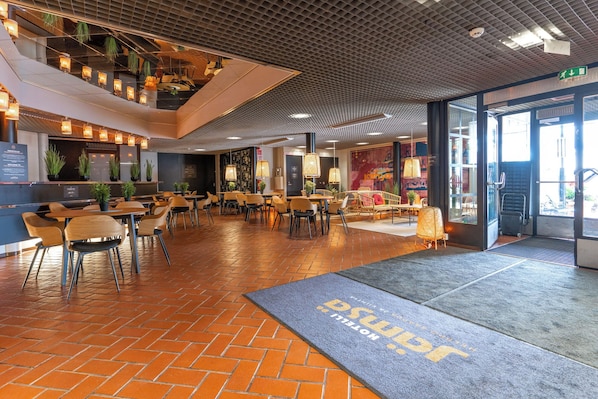 Ett rymligt inomhusområde med flera olika sittgrupper, inklusive bord och stolar, samt en receptionsdisk med en skylt.