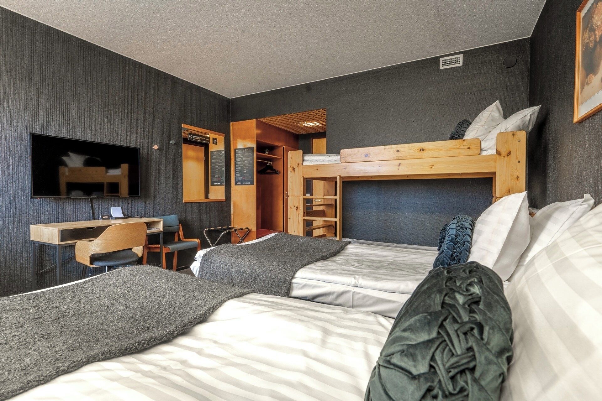 A room with bunk beds, a desk, a chair, a TV, and a wardrobe.