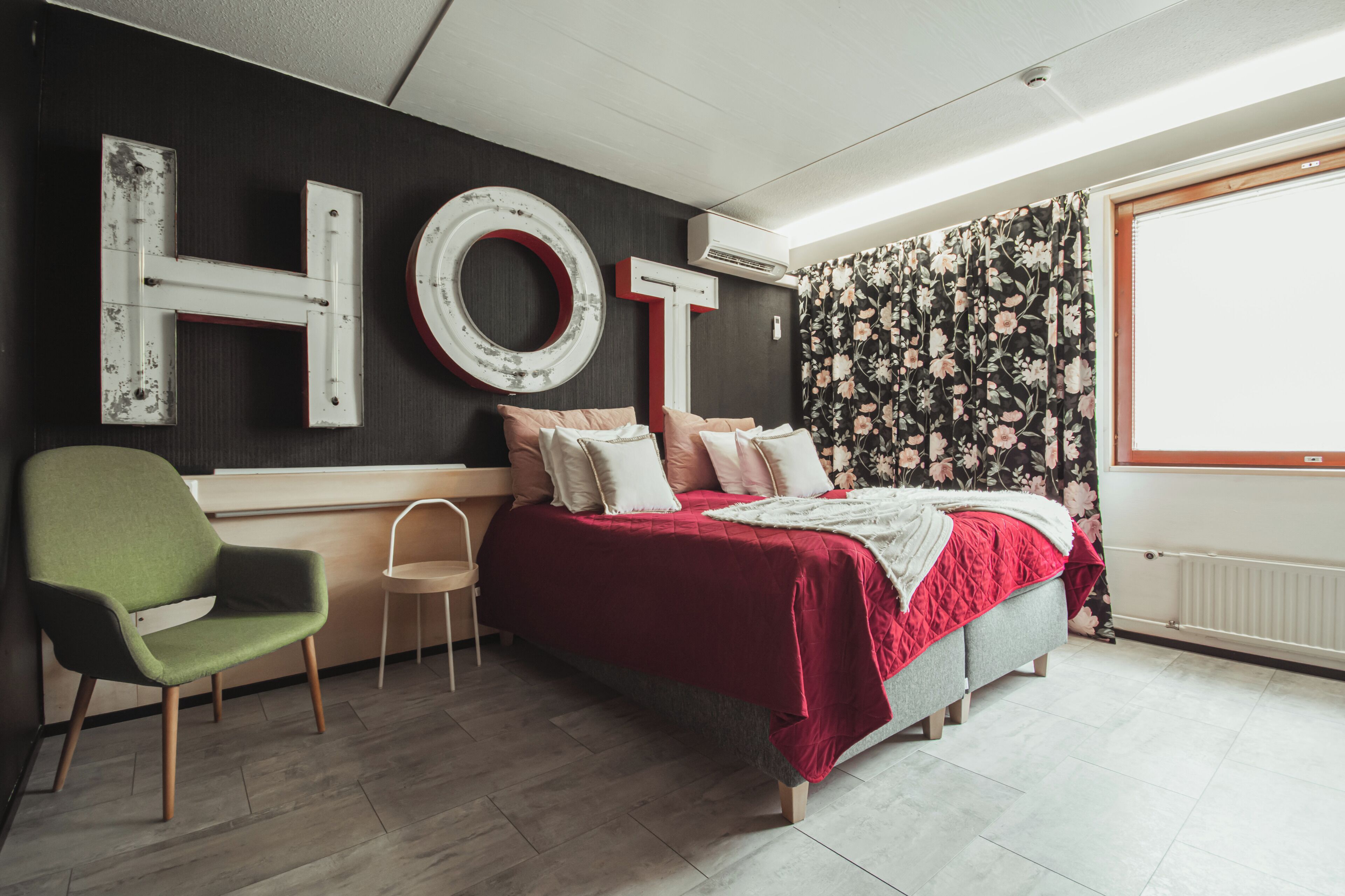 A bedroom with a bed, a green chair, a small table, and a large 'HOT' sign on the wall.