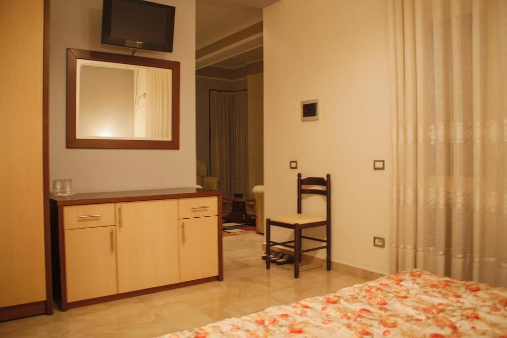 Una habitación de hotel con una cama, un aparador de madera, una silla, un televisor montado en la pared y un espejo.