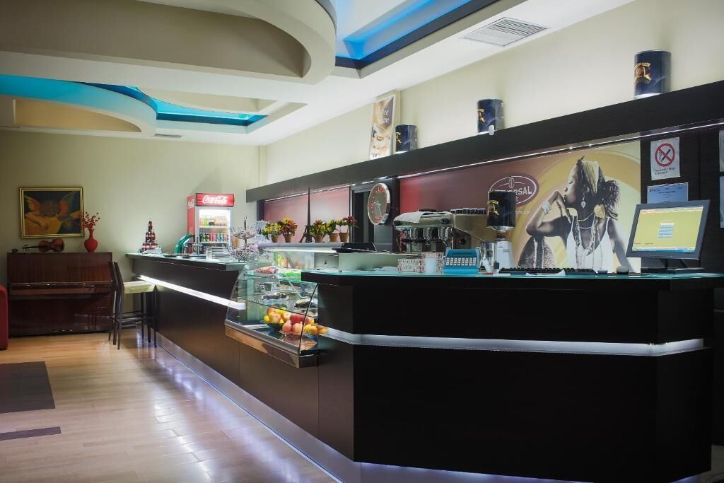 Zona de recepción de un hotel, con mostrador, refrigerador de Coca-Cola, reloj y monitor de computadora.