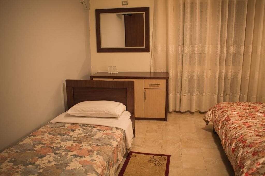 Ein Hotelzimmer mit zwei Einzelbetten, einem Holztisch, einem Spiegel und einem Fenster mit Vorhängen.