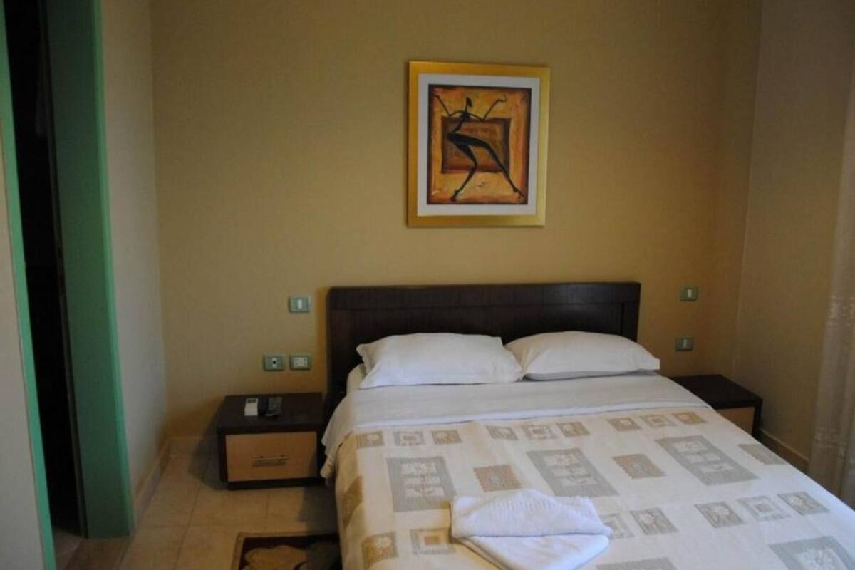 A hotel room with a bed, nightstands, a framed artwork, and a patterned bedspread.