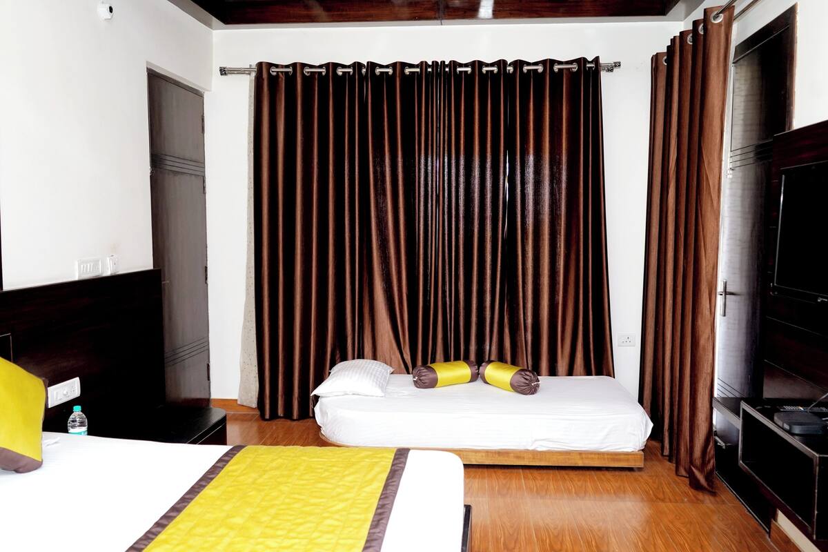 Una habitación de hotel con cama, cortinas, televisor y suelo de madera.