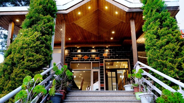 L’entrée d’un hôtel, avec une façade en bois, un comptoir d’accueil et un escalier agrémenté de plantes en pot.