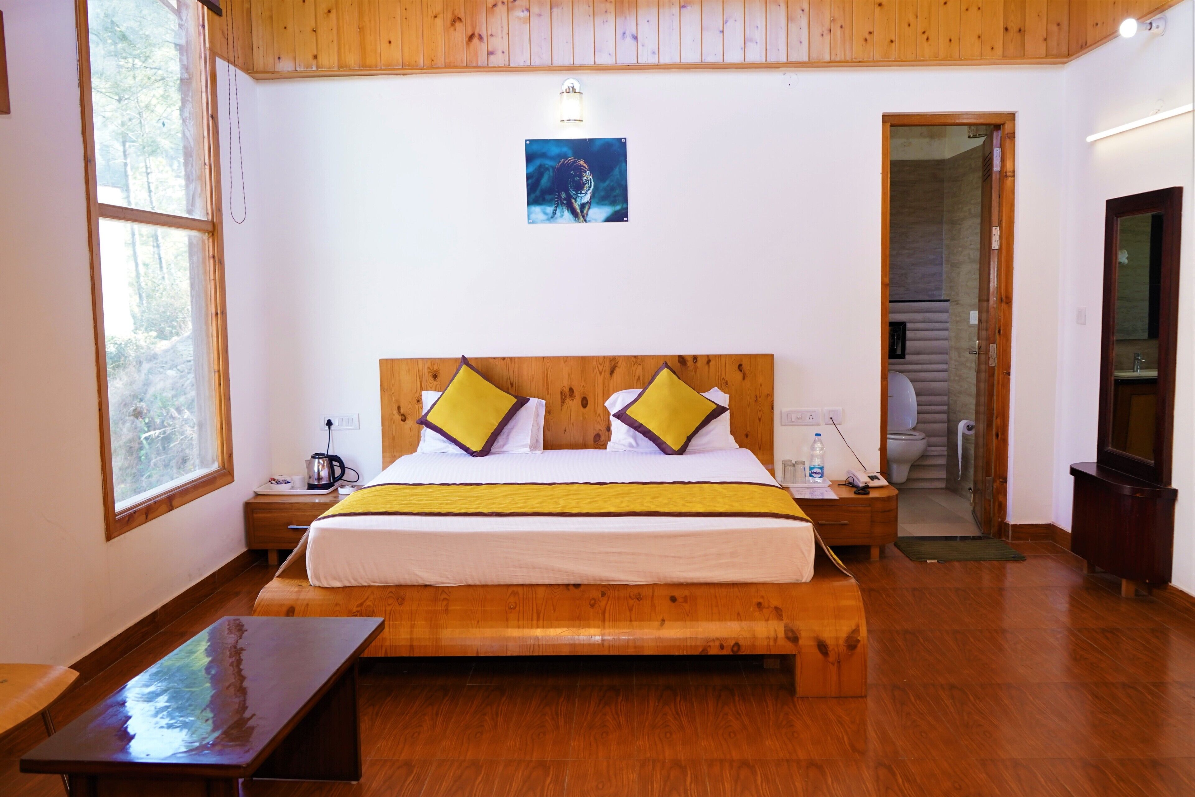 Un dormitorio con una cama de madera, dos almohadas, una mesita de noche y una puerta que da a un baño.