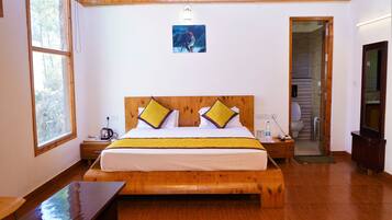 Un dormitorio con una cama de madera, dos almohadas, una mesita de noche y una puerta que da a un baño.