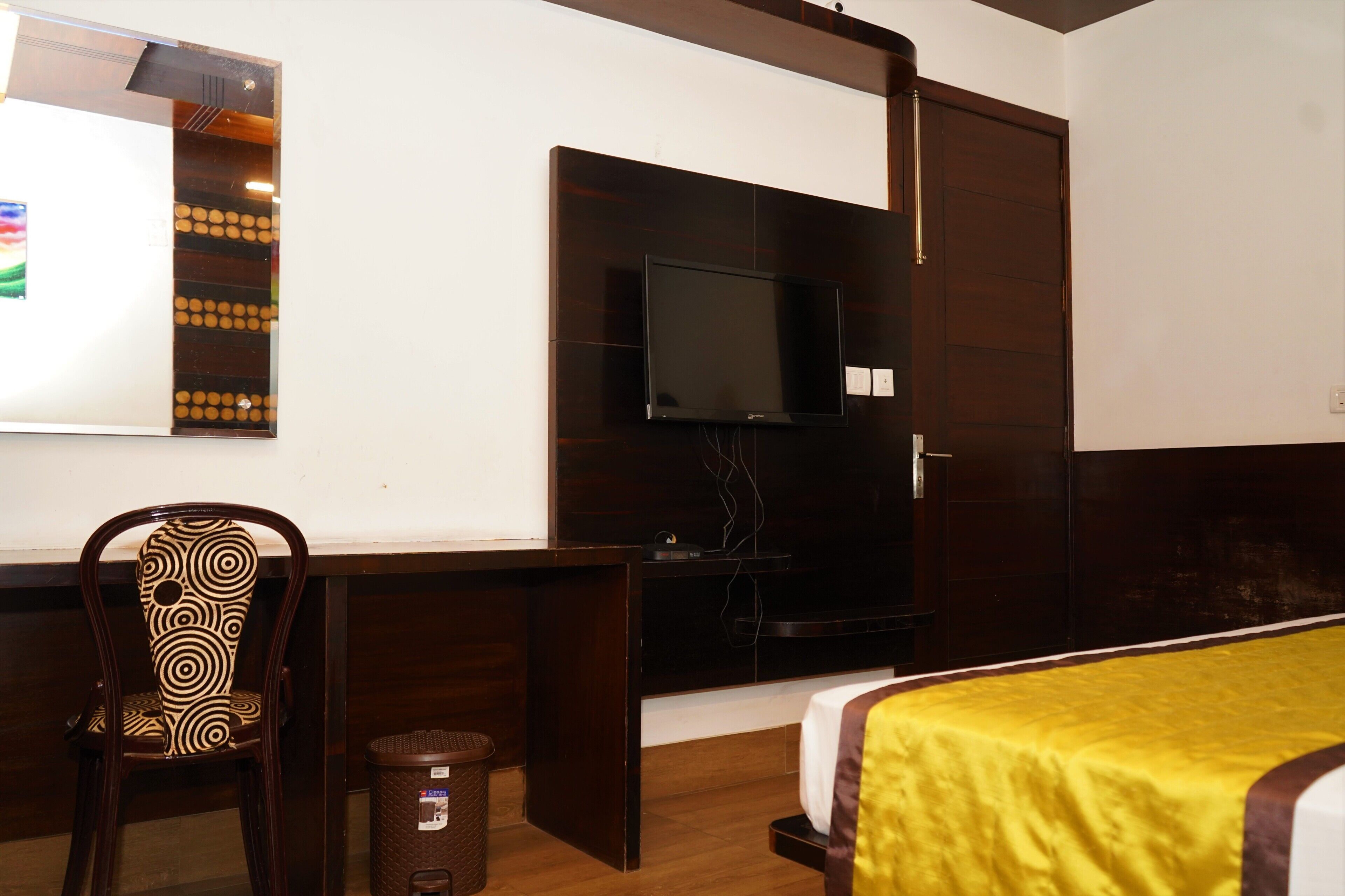 A hotel room with a bed, a desk with a chair, a television, and a small trash bin.