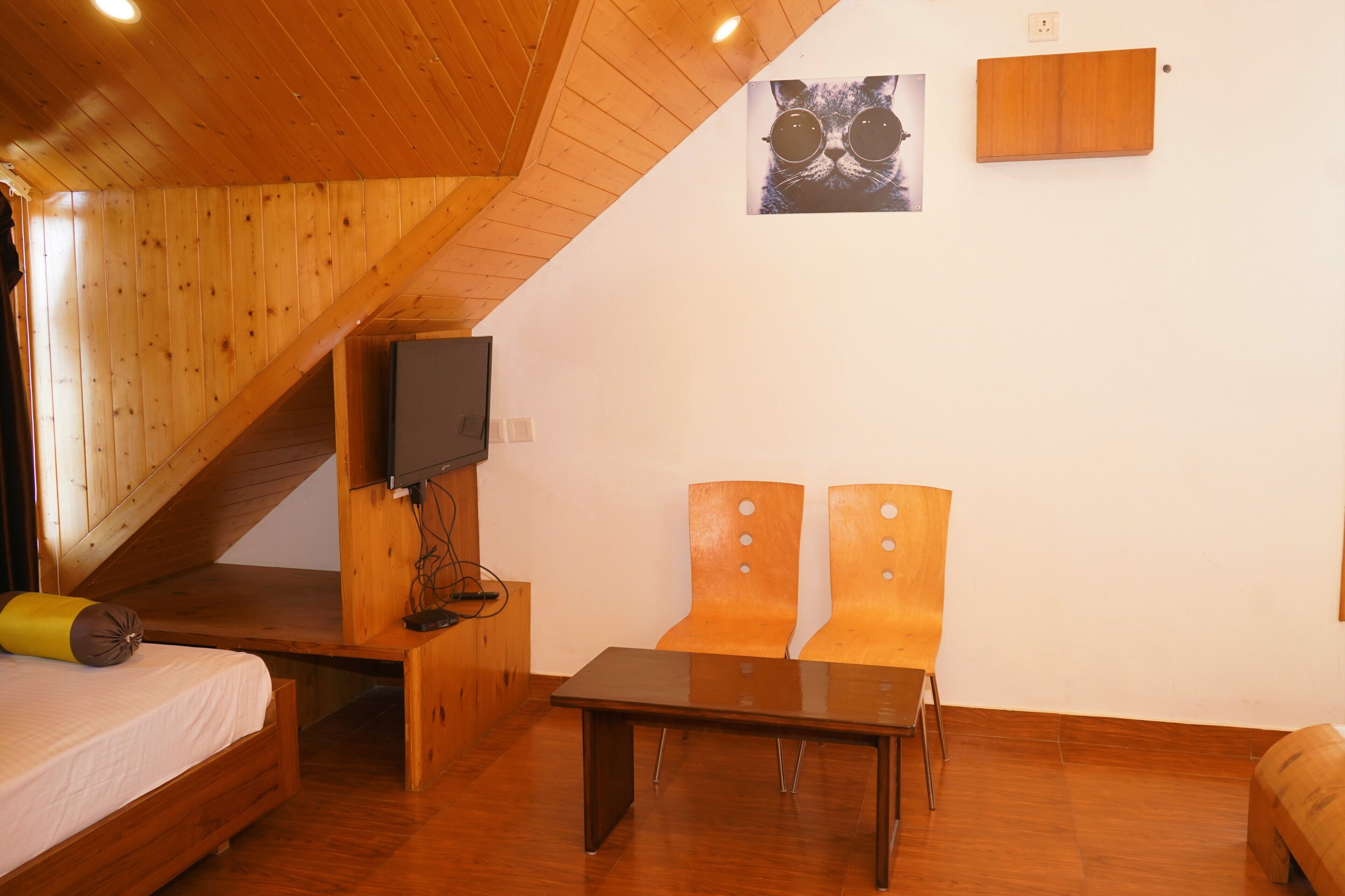 Una habitación con techo inclinado de madera, una cama, una mesa, dos sillas, un televisor y un cartel en la pared.