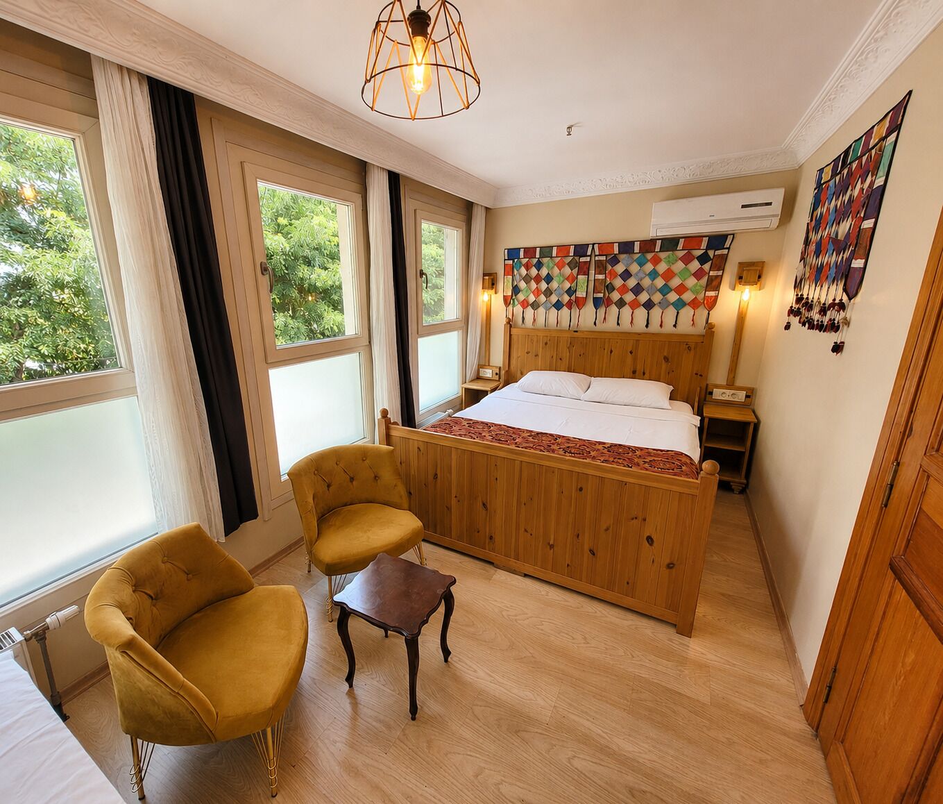 A hotel room with a wooden bed, two chairs, a small table, and a large window with curtains.