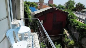 Ein Balkon mit Fliesenboden, zwei weiße Plastikstühle und ein rotes Gebäude im Hintergrund.