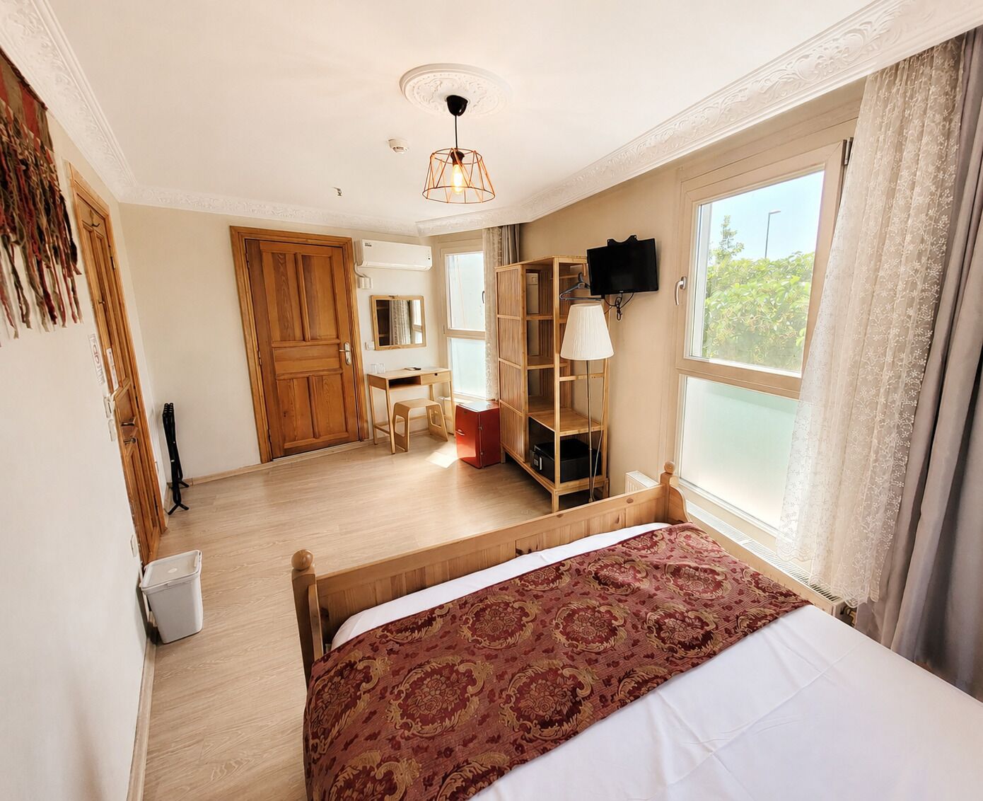 A hotel room with a bed, a desk, a wardrobe, a television, and a window with curtains.