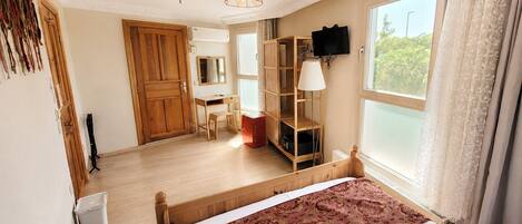 A hotel room with a bed, a desk, a wardrobe, a television, and a window with curtains.