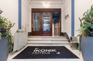 Ein Hotel Eingang mit schwarzer Fußmatte, Doppeltüren und einem Schild für 'Ikonik Hotels'.