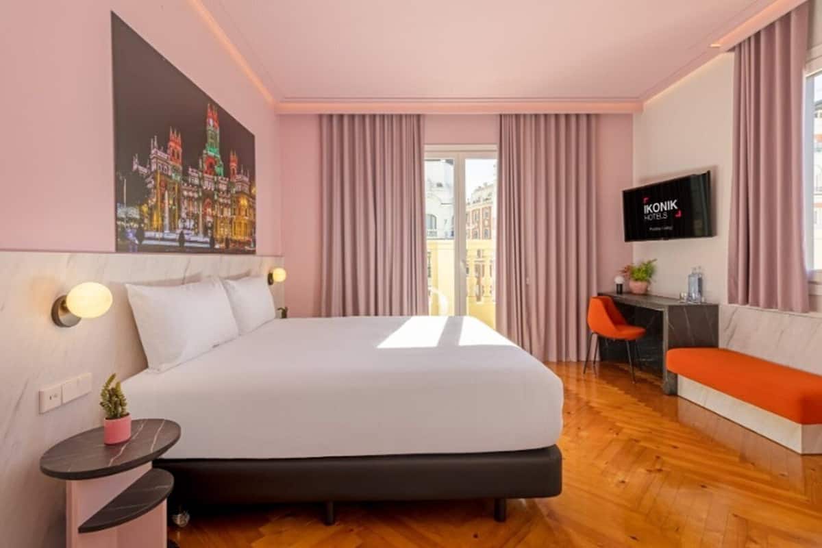 A modern hotel room with a large bed, a desk, a TV, and a balcony view.