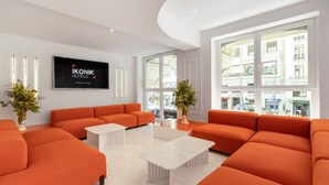 A modern hotel lobby with orange sofas, a flat-screen TV, and large windows offering city views. - Ikonik Gran Via (Madrid)