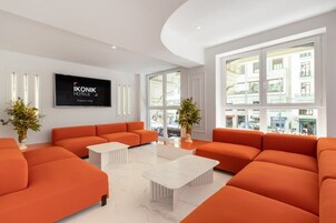 Eine moderne Hotelhalle mit orangefarbenen Sofas, einem Flachbildfernseher und großen Fenstern mit Blick auf die Stadt.