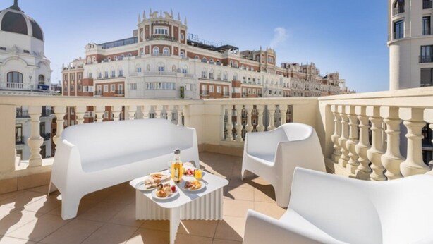 A rooftop terrace with white furniture, a table with food, and a view of historic buildings. - Ikonik Gran Via (Madrid)