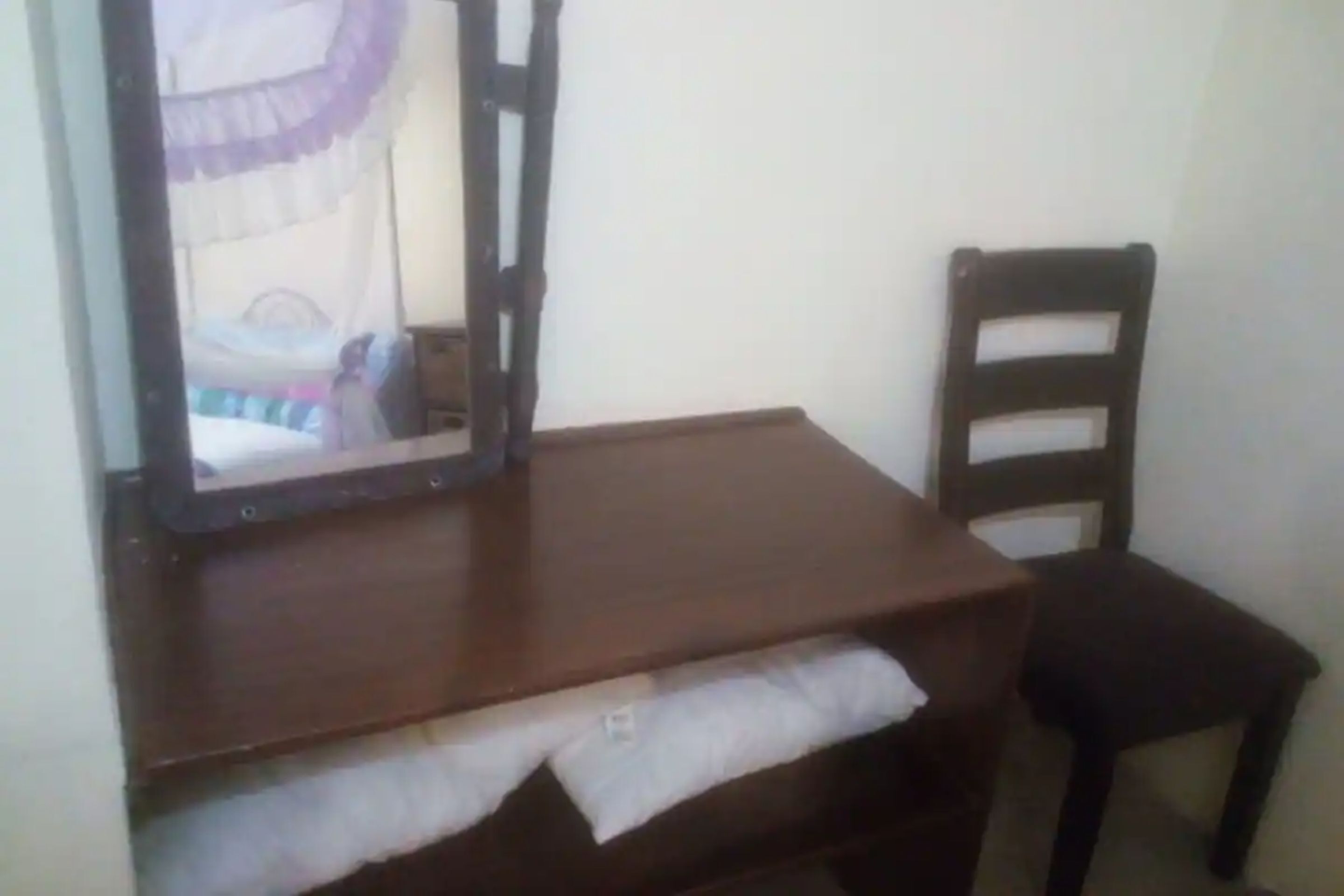Une petite commode en bois foncé, avec un miroir et une chaise.